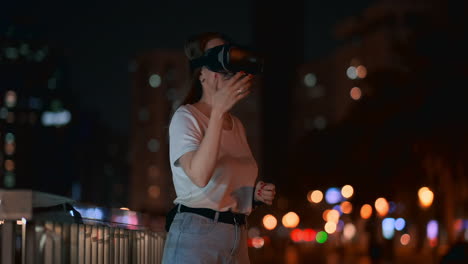 A-young-woman-in-virtual-reality-glasses-in-the-night-city-moves-her-hands-mastering-the-application-interface.-VR-technologies-of-the-future-in-everyday-life.-Virtual-reality-games
